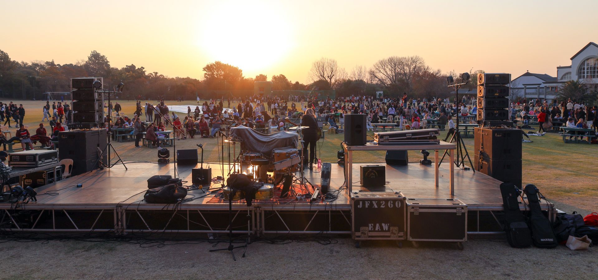 A large crowd of people are gathered around a stage in a field at sunset.
