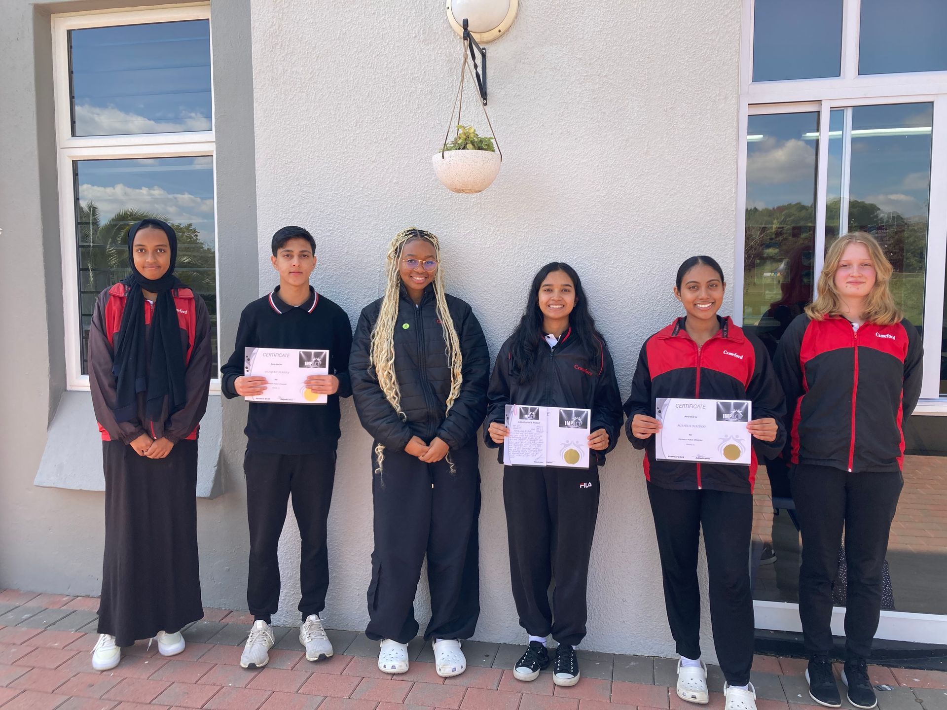 A group of young people are standing in front of a building holding certificates.
