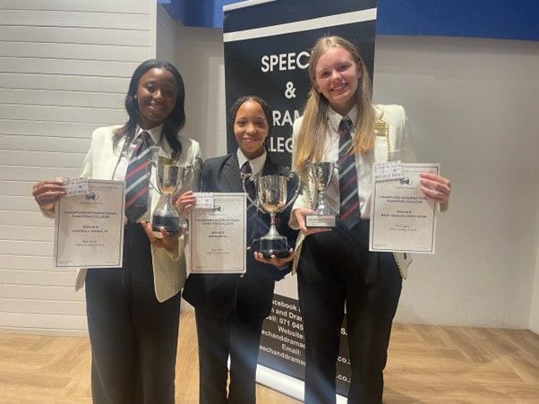 Three girls in school uniforms are holding trophies and certificates.