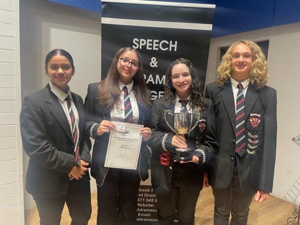 A group of young people are standing next to each other in front of a sign that says speech and grammar.