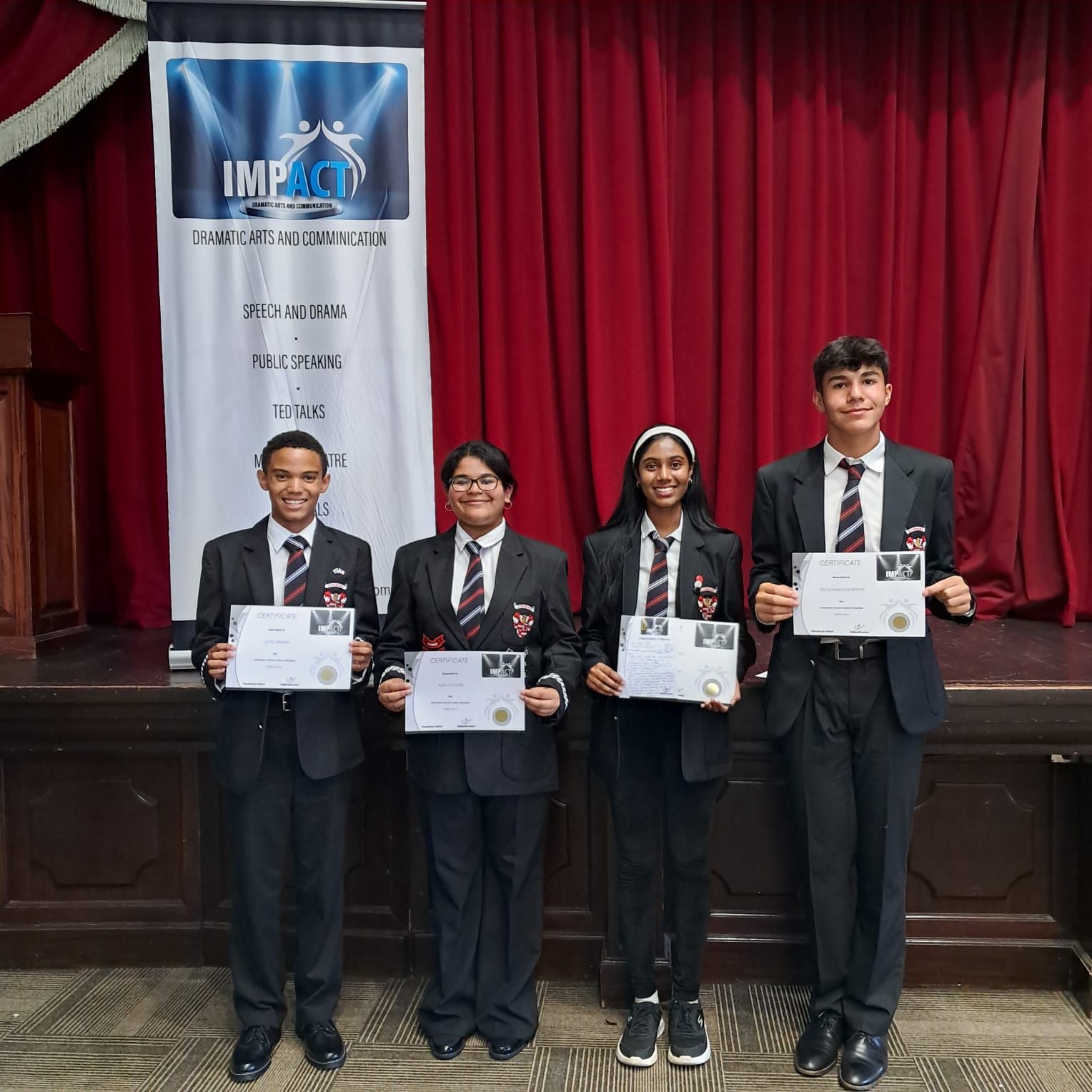 A group of people in suits and ties are standing in front of a red curtain holding certificates.