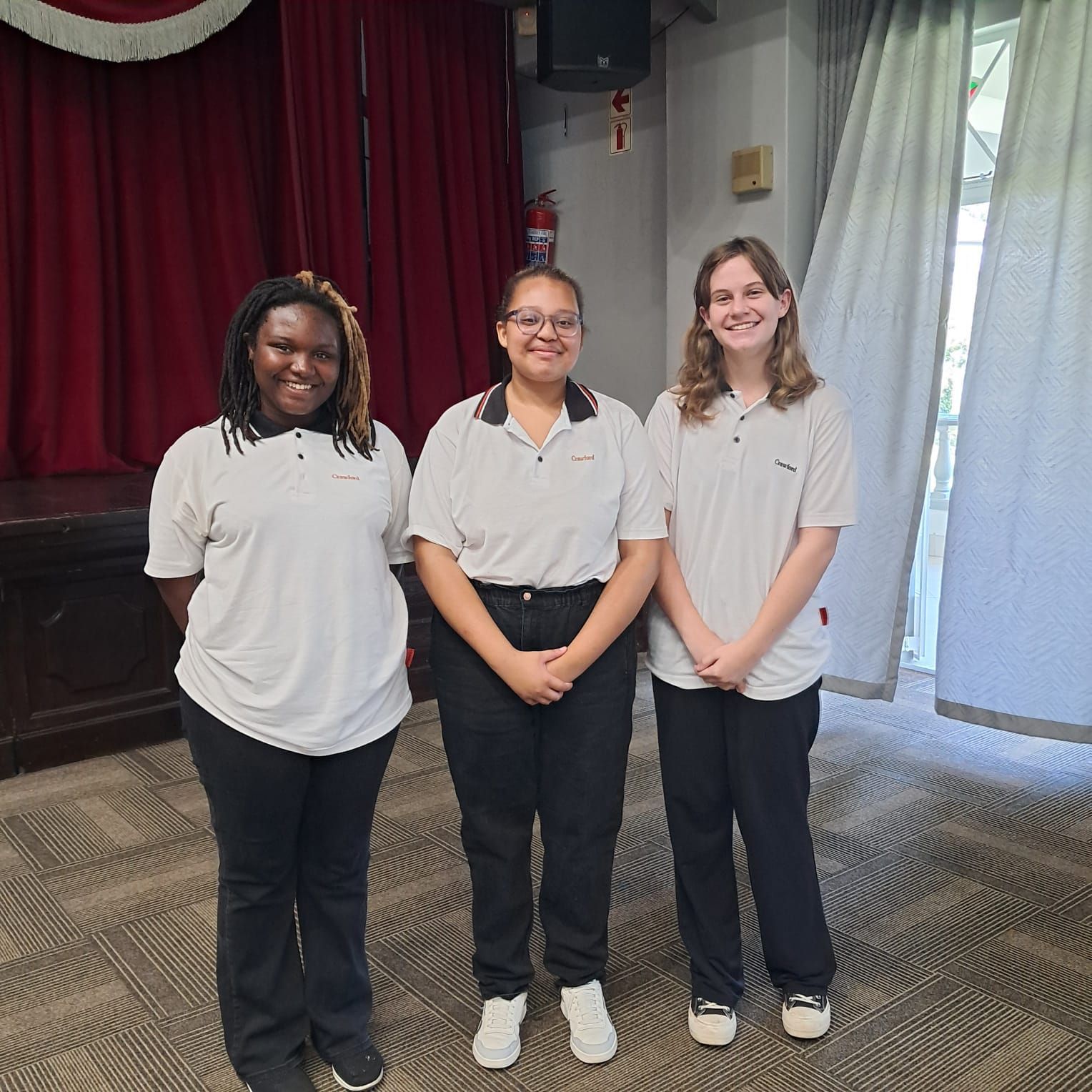 Three girls are posing for a picture in front of a red curtain
