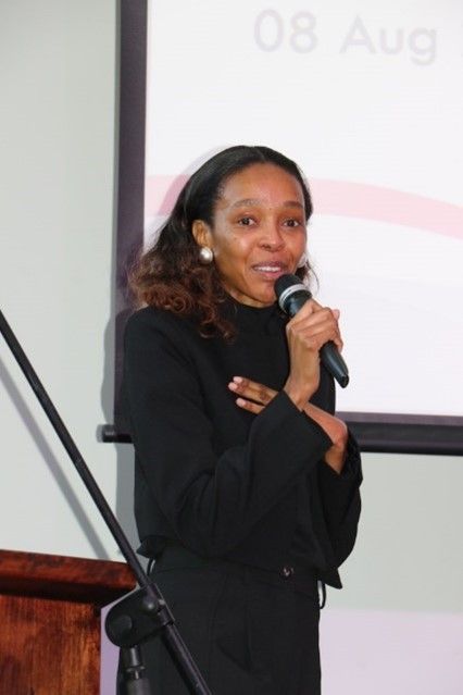 A woman is holding a microphone in front of a screen that says 08 aug