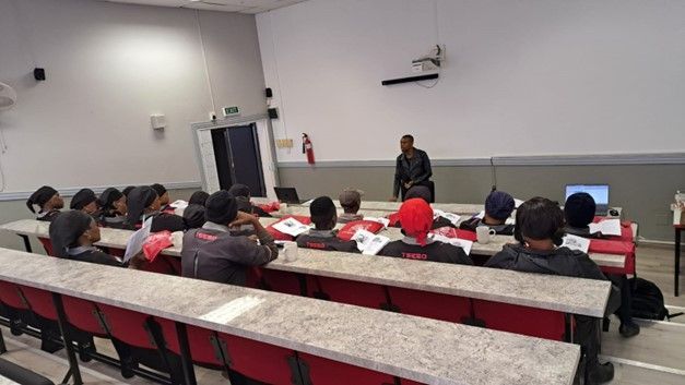 A group of people are sitting at long tables in a lecture hall.