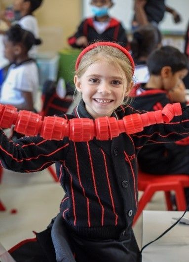 A little girl in a black and red striped shirt is holding a string of red beads.