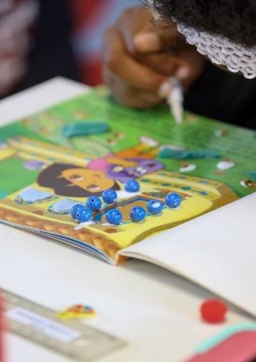 A person is drawing a picture in a book with blue beads