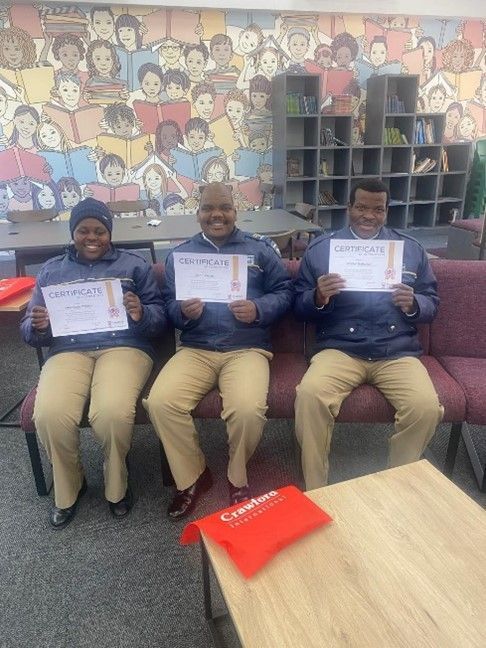 Three people are sitting on a bench holding certificates