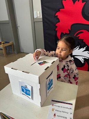 A little girl is putting a vote in a ballot box.