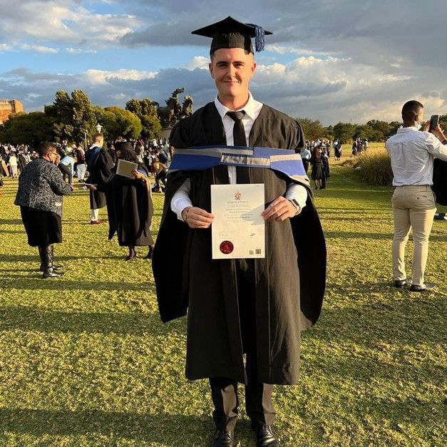 A man in a graduation cap and gown is holding a diploma.