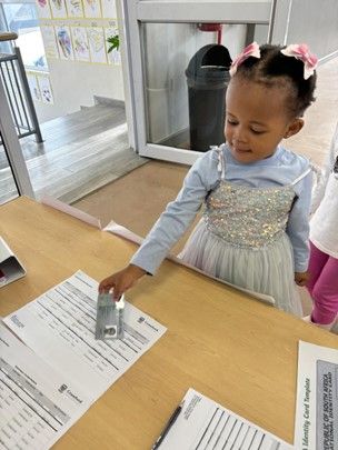 A little girl is sitting at a table holding a piece of paper.