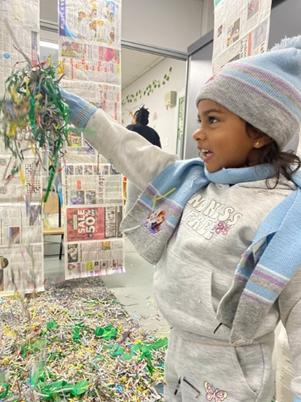 A little girl wearing a hat and scarf is playing with confetti.