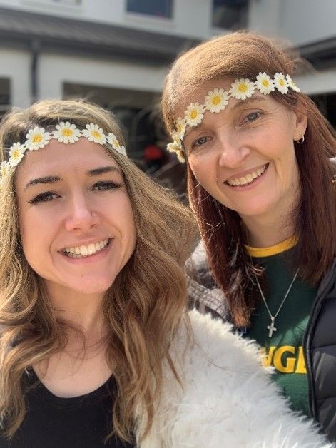 Two women wearing flower crowns on their heads are smiling for a picture.