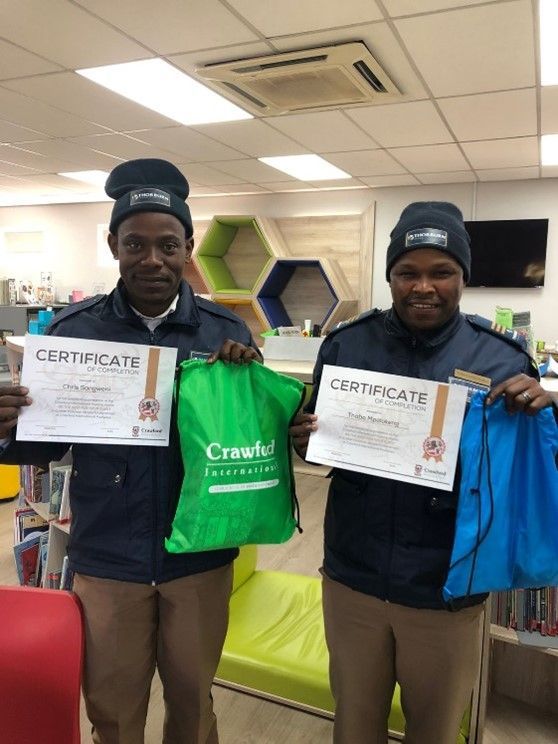 Two men are holding up certificates and bags in a room.