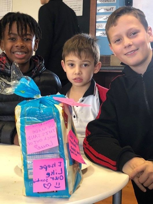 Three young boys standing next to a bag of bread