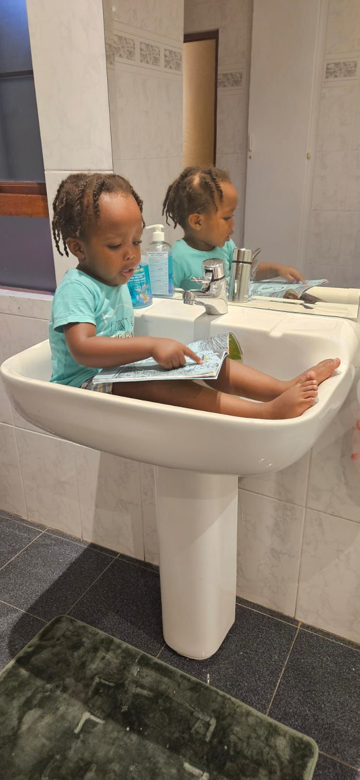 A little girl is sitting in a bathroom sink.