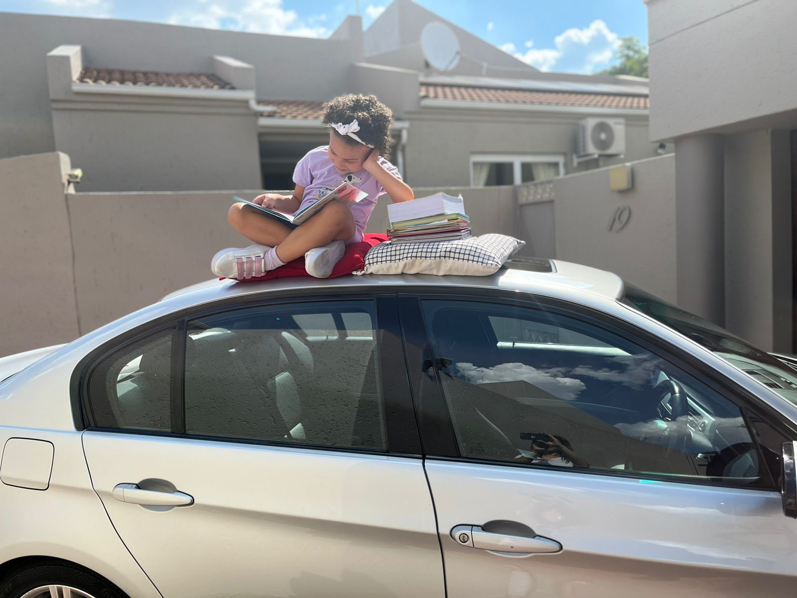 A little girl is sitting on the roof of a car