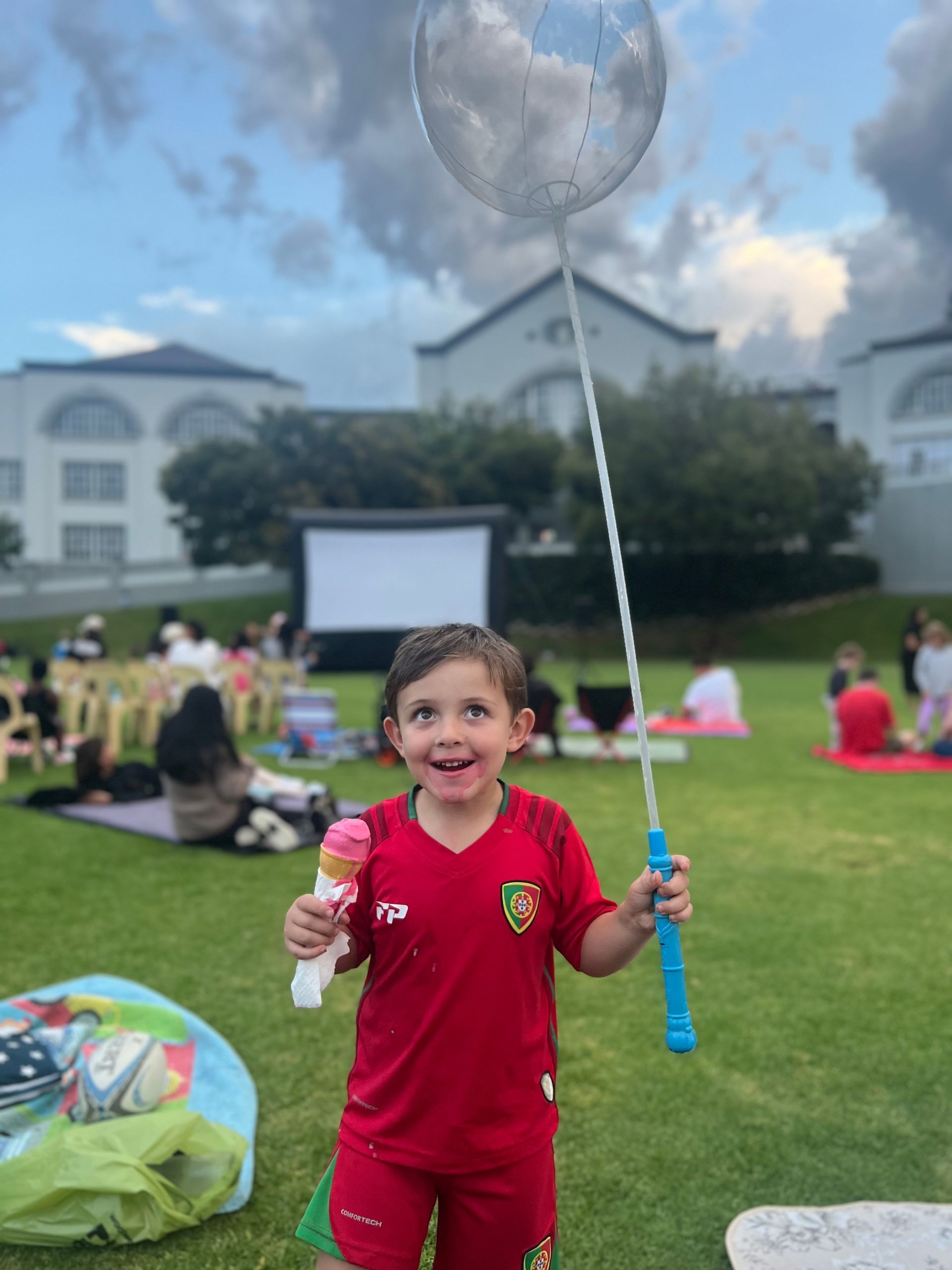 A little boy in a red shirt is holding a balloon and soap bubbles.