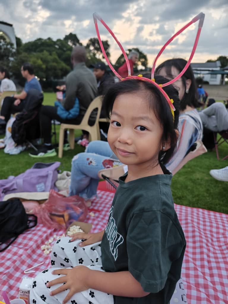 A little girl wearing bunny ears is sitting on a picnic blanket.