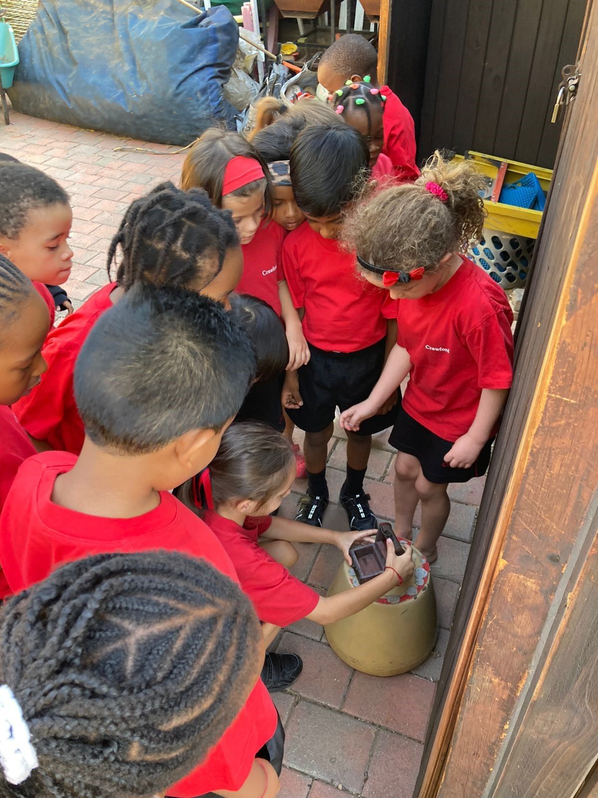 A group of children in red shirts are standing around a bucket.