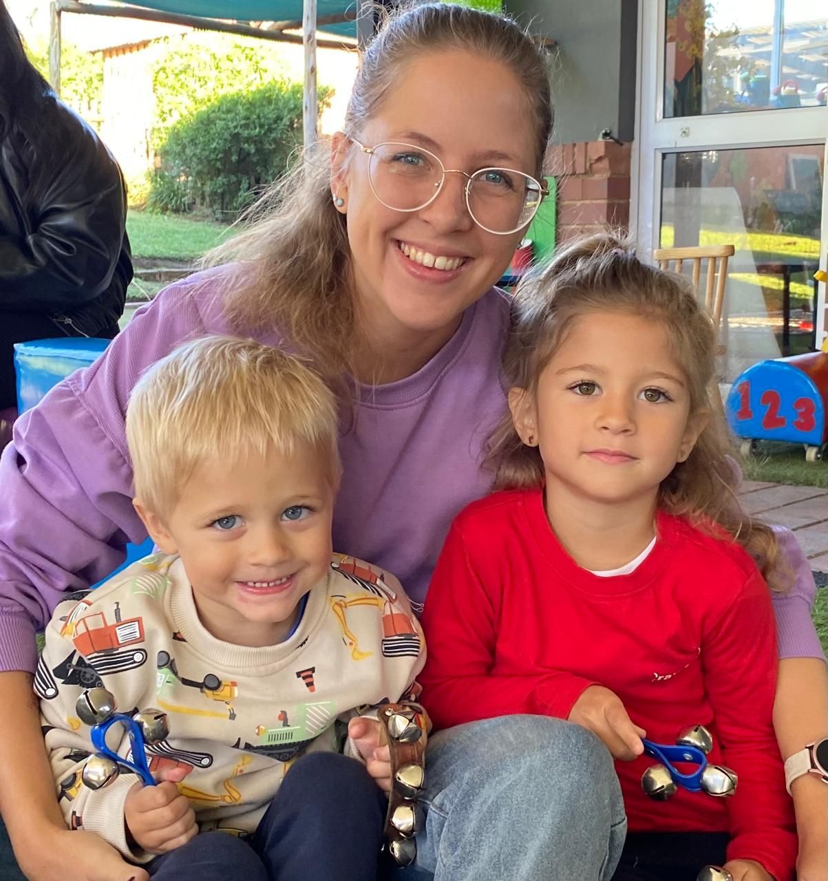 Woman smiling with two children, all holding scissors, outdoors.