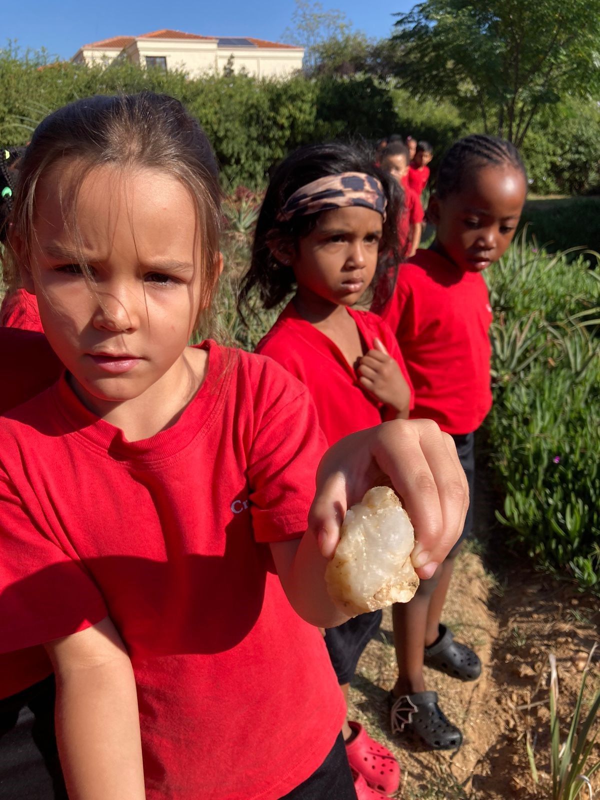 A girl in a red shirt is holding a rock in her hand.
