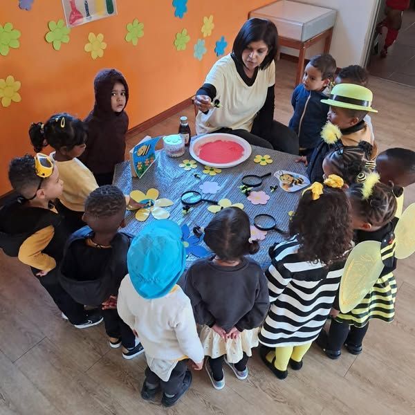 Children in bee costumes watch a teacher conduct a science experiment at a table.