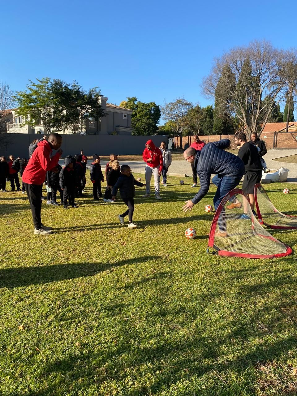 Soccer practice on a sunny field. A coach sets up small goals; children and adults watch.