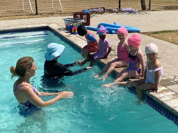 A group of children are sitting on the edge of a swimming pool.
