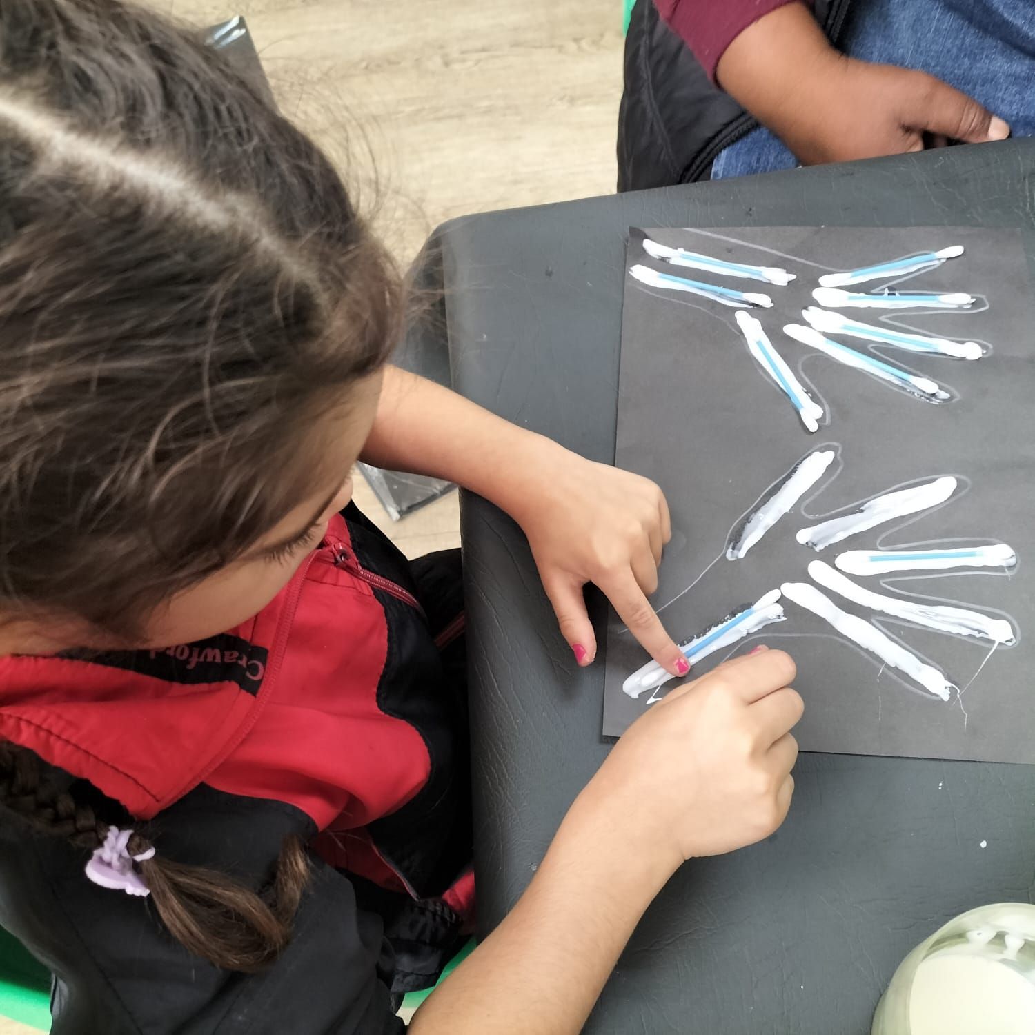A little girl is sitting at a table drawing with chalk
