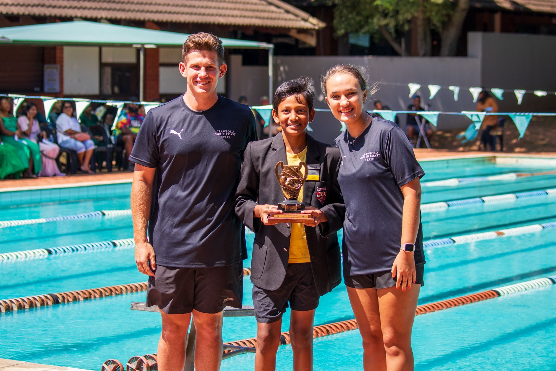 A group of people standing next to a swimming pool holding a trophy.