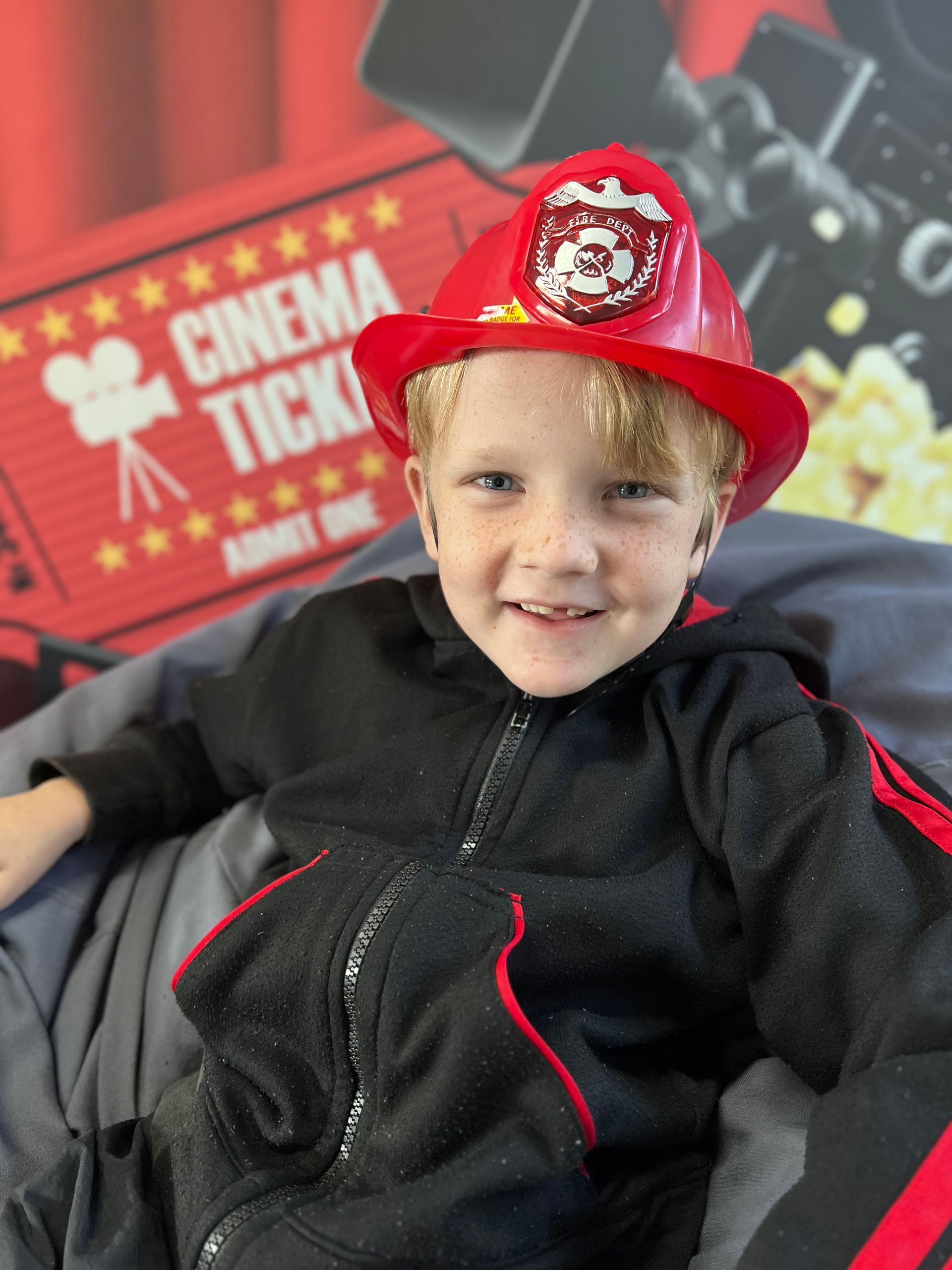 A little boy wearing a fireman costume is sitting in a chair.