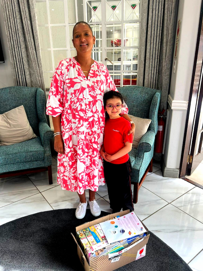 A woman in a pink dress is standing next to a boy in a living room.