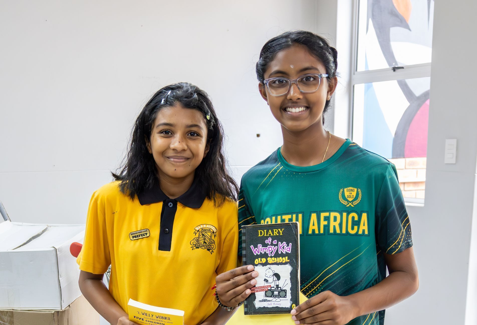 Two young girls are standing next to each other holding books.