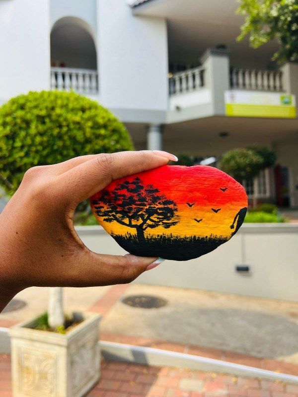 A person is holding a rock with a painting of a tree on it.