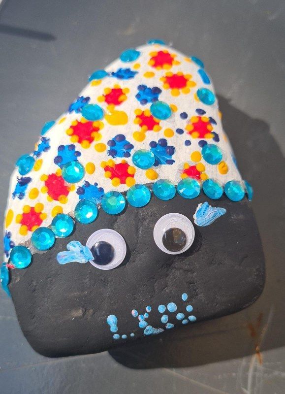 A black rock with googly eyes and a colorful hat