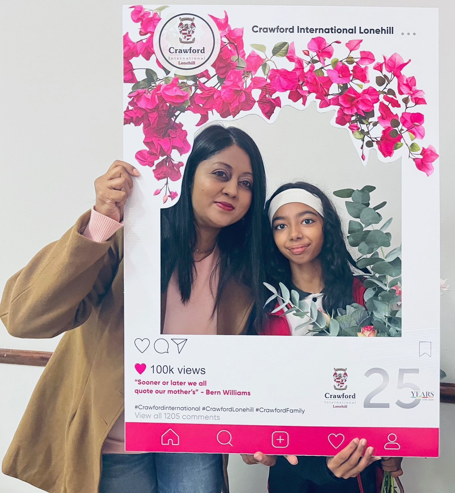 Two people pose behind a large social media-style cutout with flowers.
