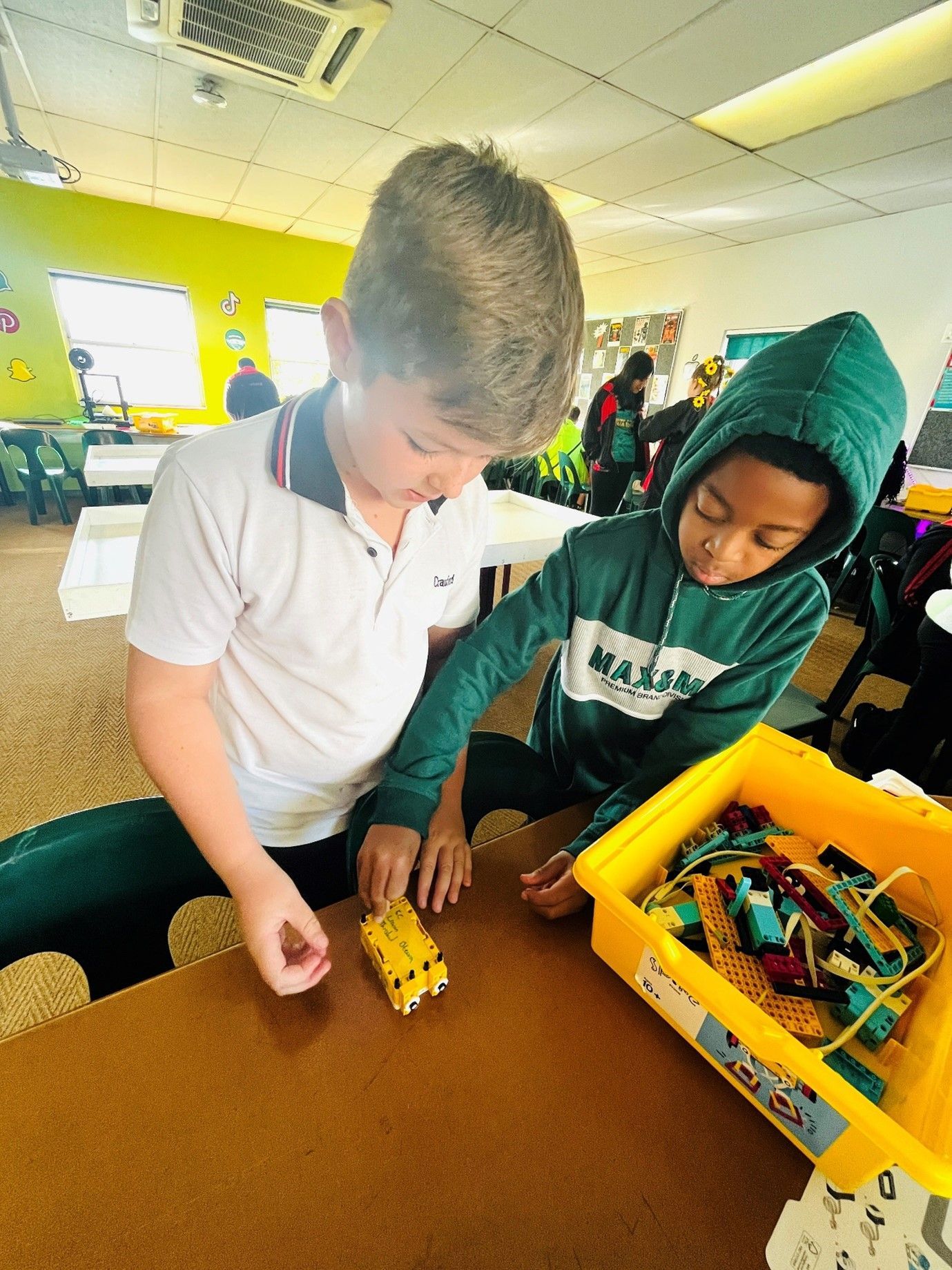 Two young boys are playing with a toy car on a table.