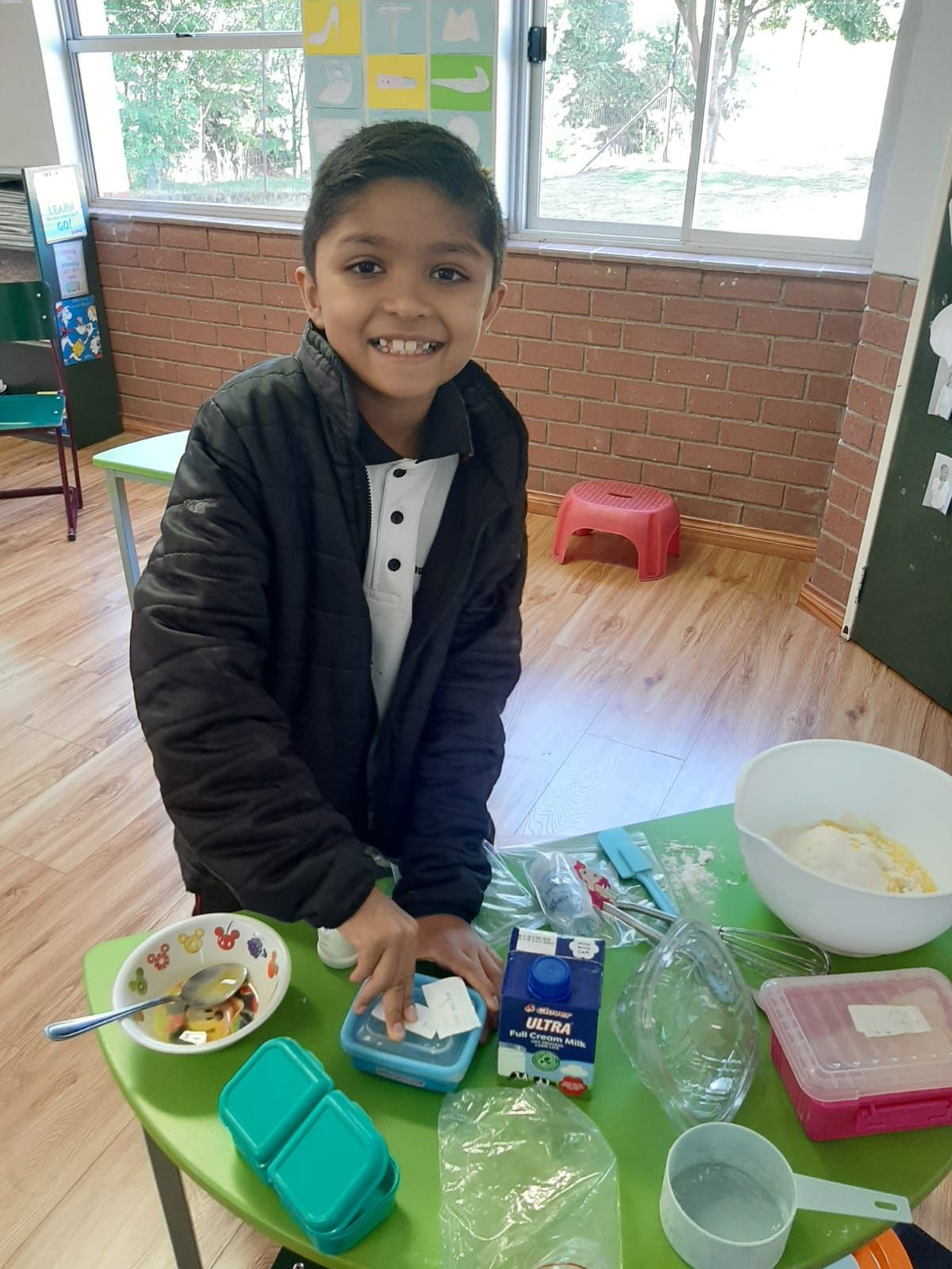 A young boy is sitting at a table with a bowl of food and a carton of milk.