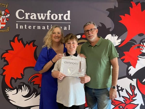 A boy is holding a certificate in front of a crawford international sign