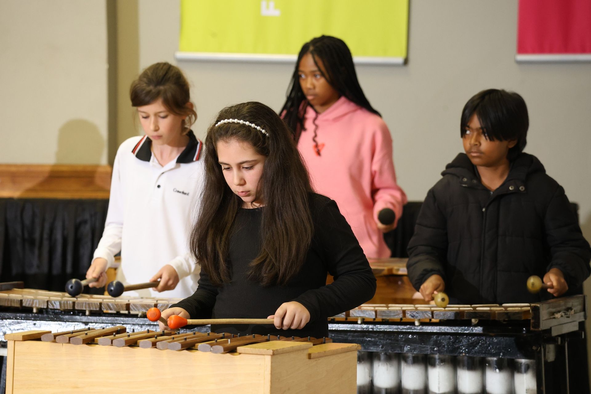 Four children playing xylophones with mallets in a well-lit room.