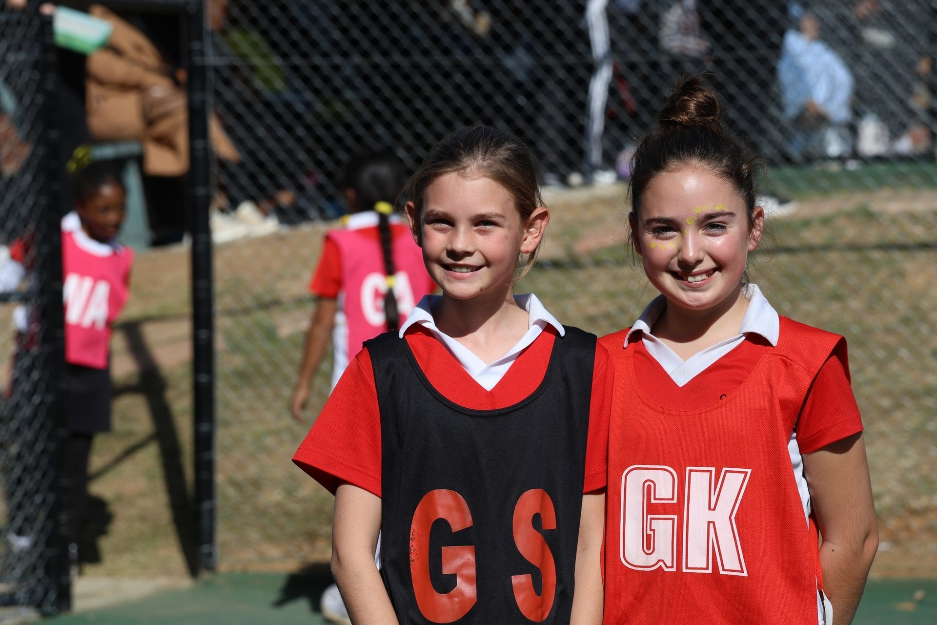 Two girls in red and black netball bibs smile at the camera.