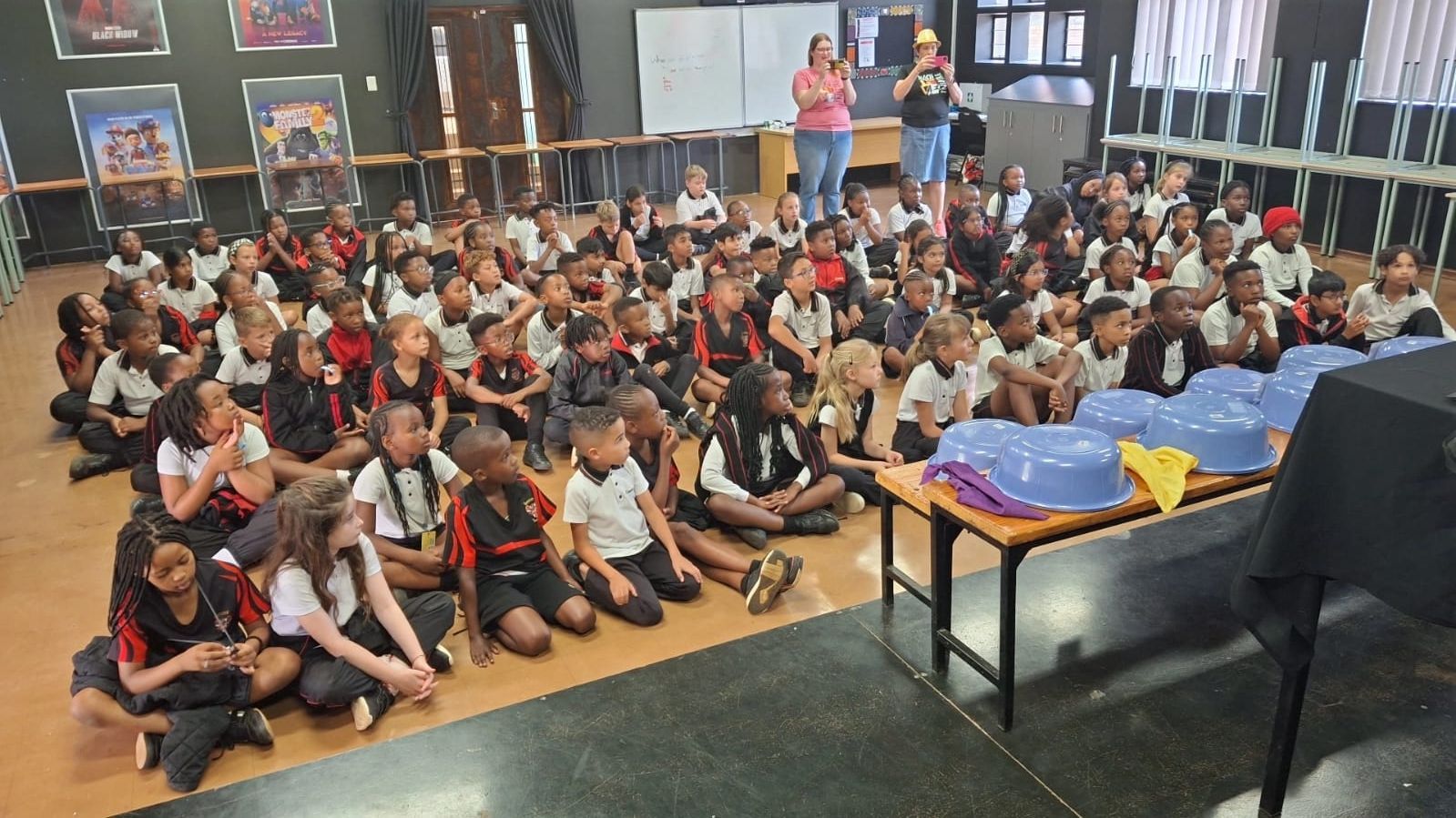 A large group of children are sitting on the floor in a room.