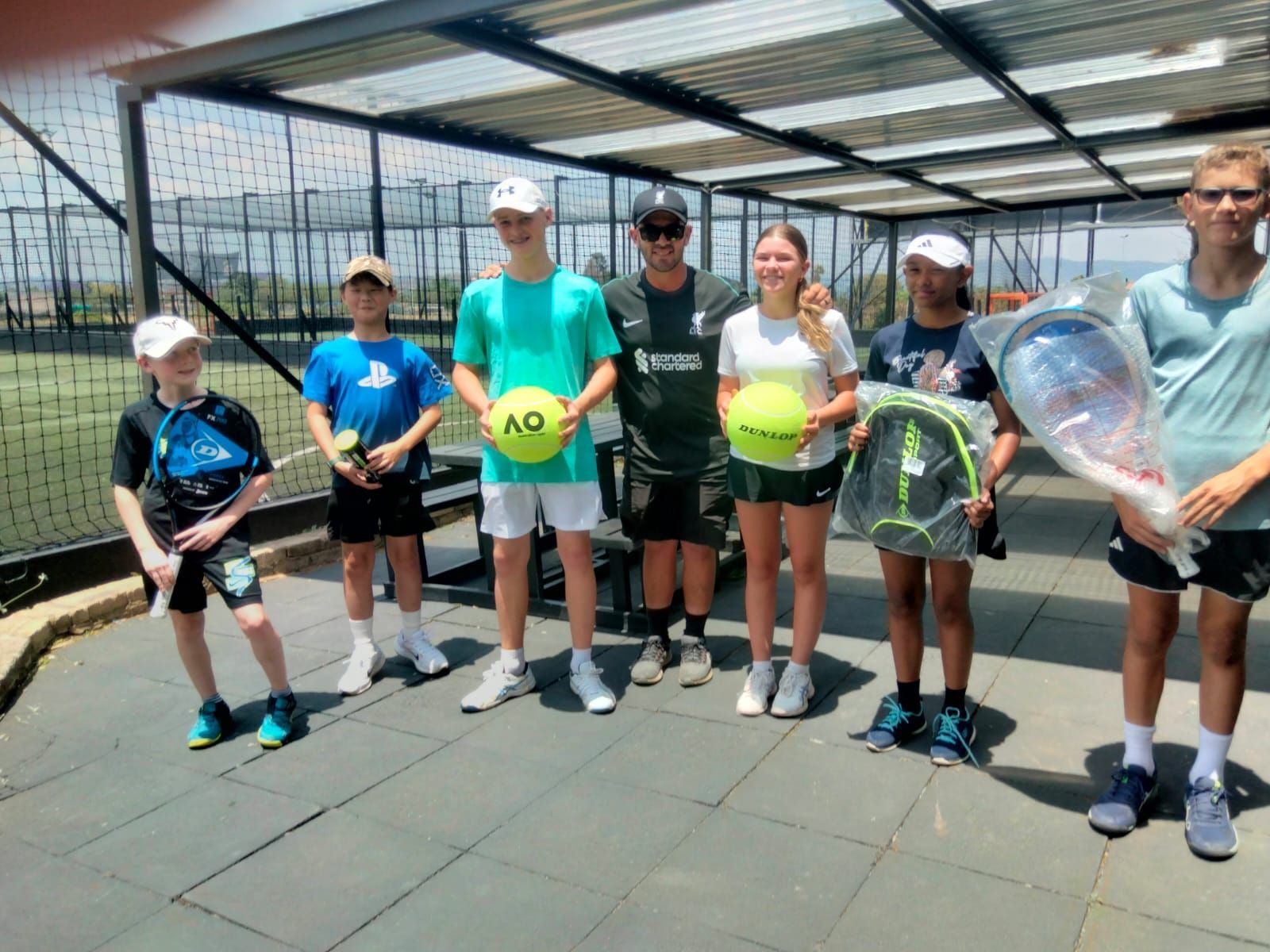 A group of young people standing next to each other holding tennis rackets and tennis balls.