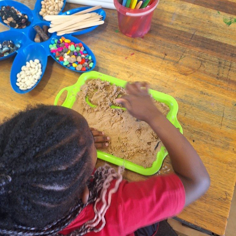 A little girl is playing with sand on a green tray