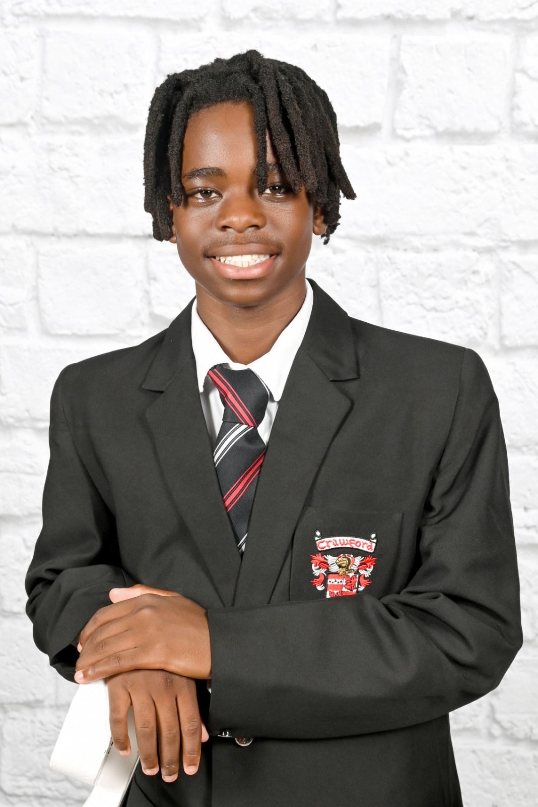 Student in school uniform smiling, standing in front of a white brick wall.