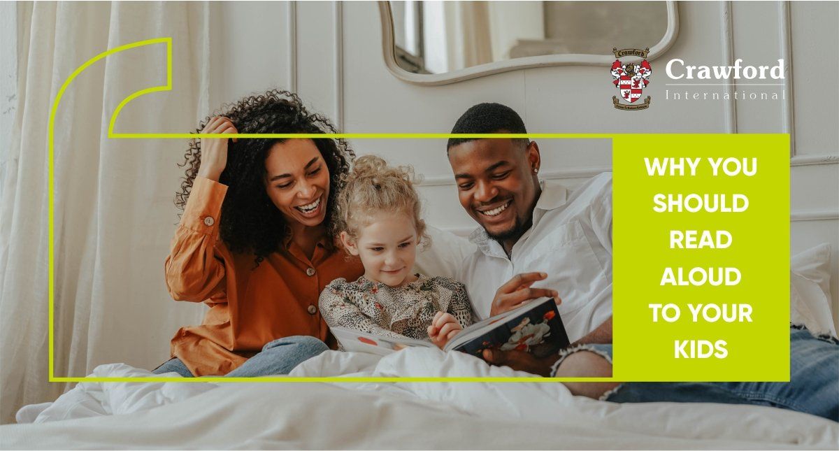 A family is sitting on a bed reading a book together.