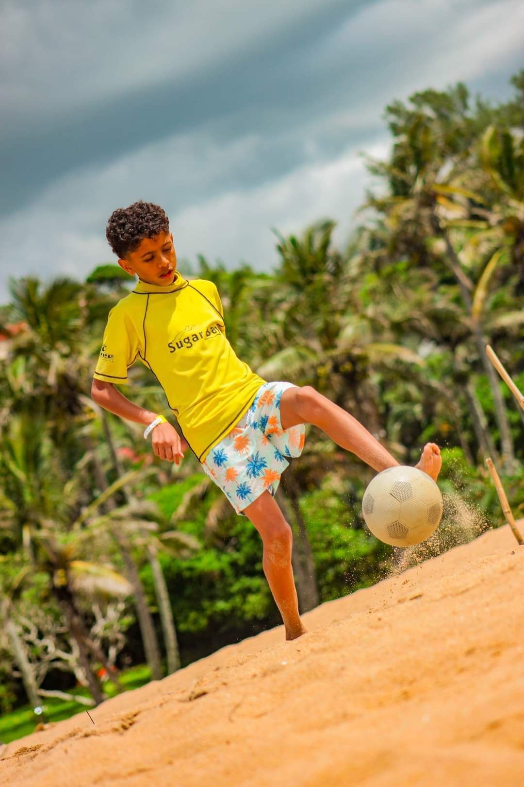 A young boy is kicking a soccer ball on the beach.