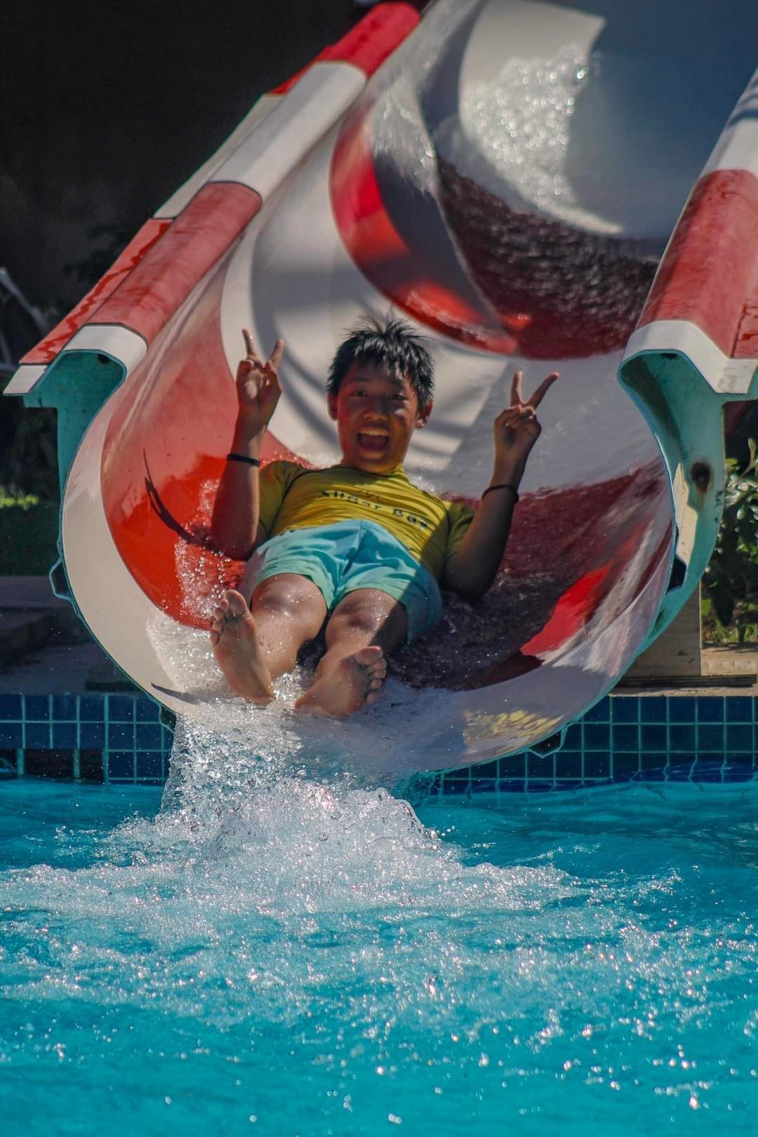 A young boy is sliding down a water slide in a swimming pool.