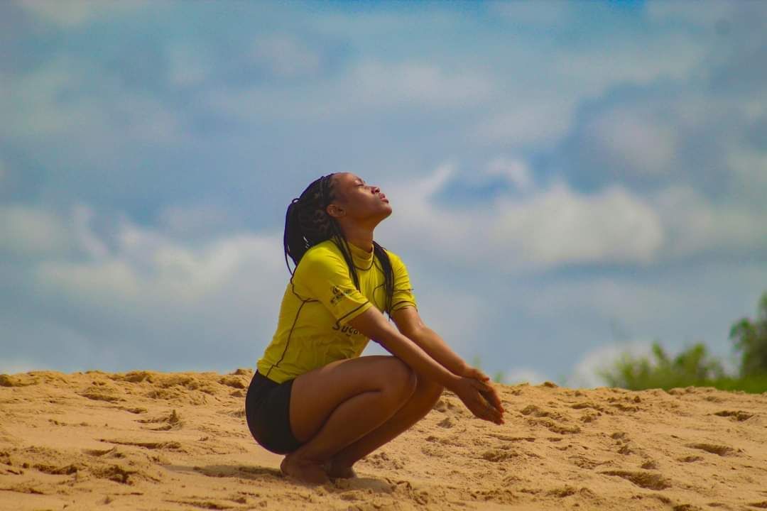 A woman is squatting on a sandy beach looking up at the sky.