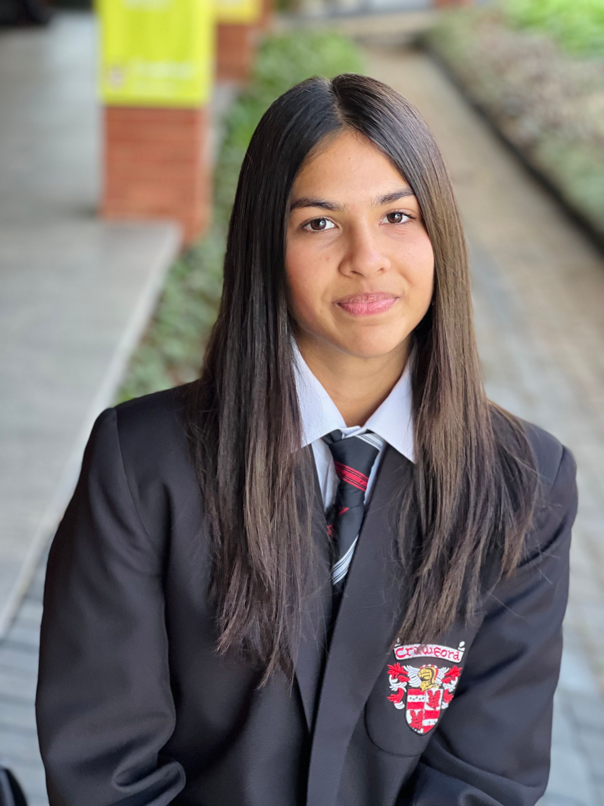 A young woman in a suit and tie is sitting on a sidewalk.